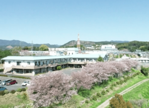 桜の木に囲まれた介護施設の建物外観。広々とした敷地に立つ平屋造りの施設